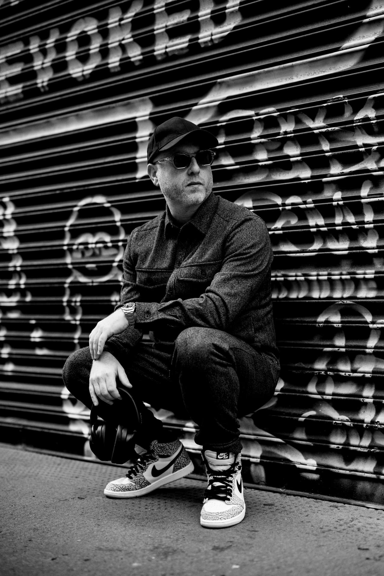 Biblical Beats crouched against a graffiti shutter, black and white